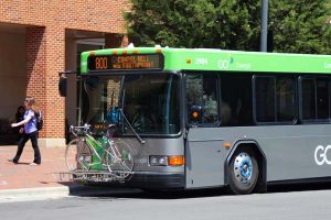 GoTriangle bus with a bike attached to the front dropping a student off in front of a brick building dropping a student off